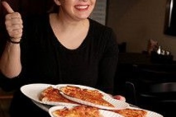Woman holding pizza slices on plates, giving a thumbs up in a dimly lit room.