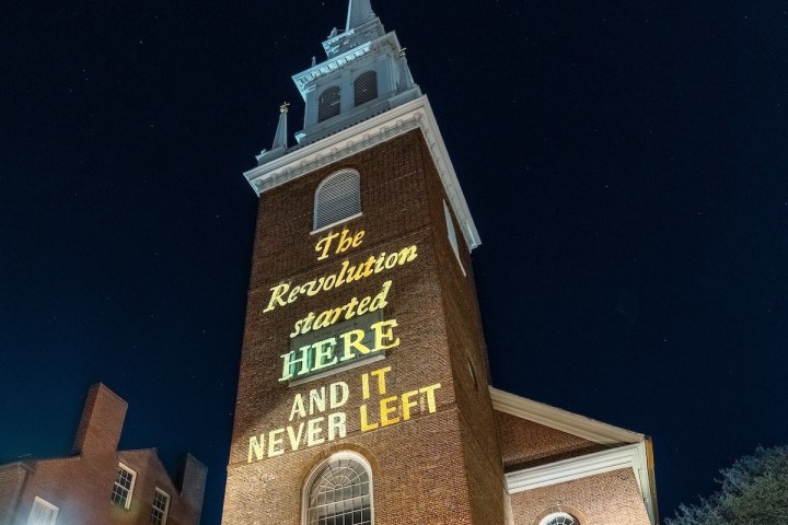 Brick church steeple illuminated with text: 'The Revolution started HERE AND IT NEVER LEFT.'